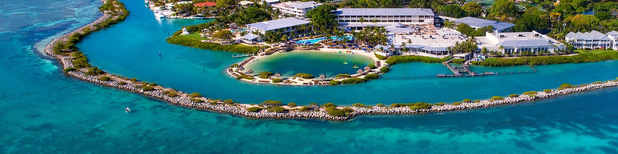 Aerial view of a coastal town surrounded by turquoise waters, featuring buildings, a lagoon, and a natural marine environment.