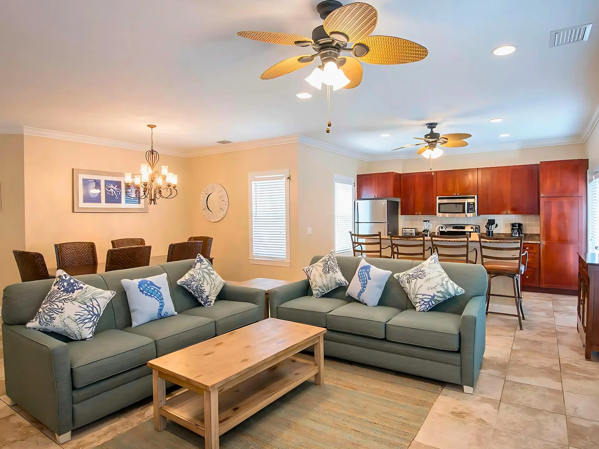 Open-concept living and kitchen area with greenish-gray sofas, wooden dining set, and ceiling fans.