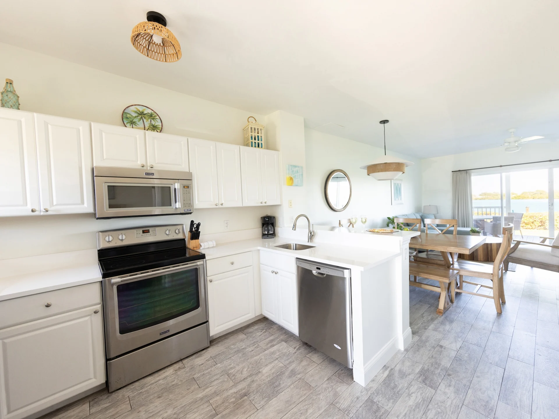 Coastal kitchen and dining area with white cabinets, wooden table, pendant light, and balcony water view.