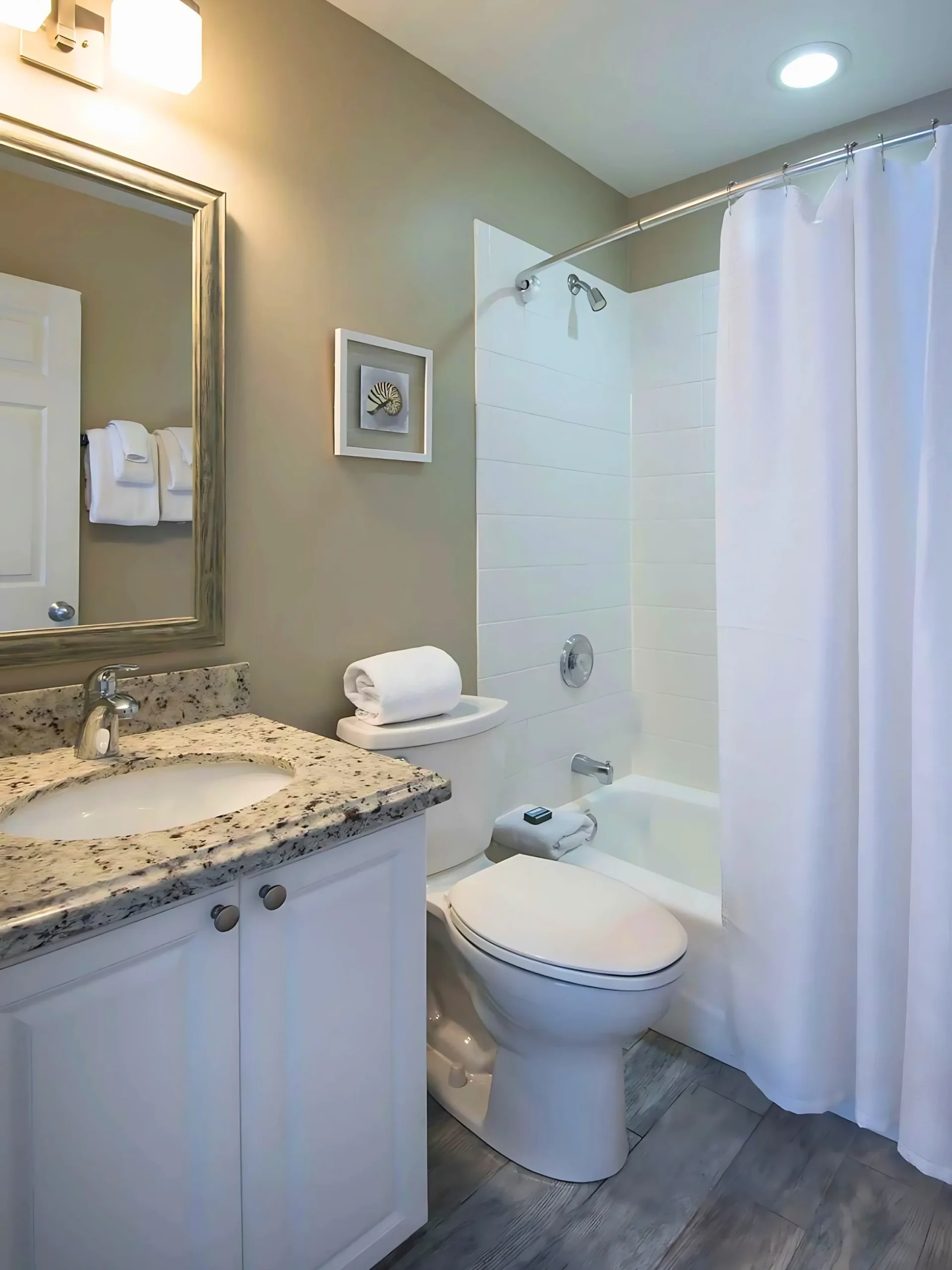 Modern bathroom with granite countertop, white vanity, shower curtain, and coastal-themed wall decor.