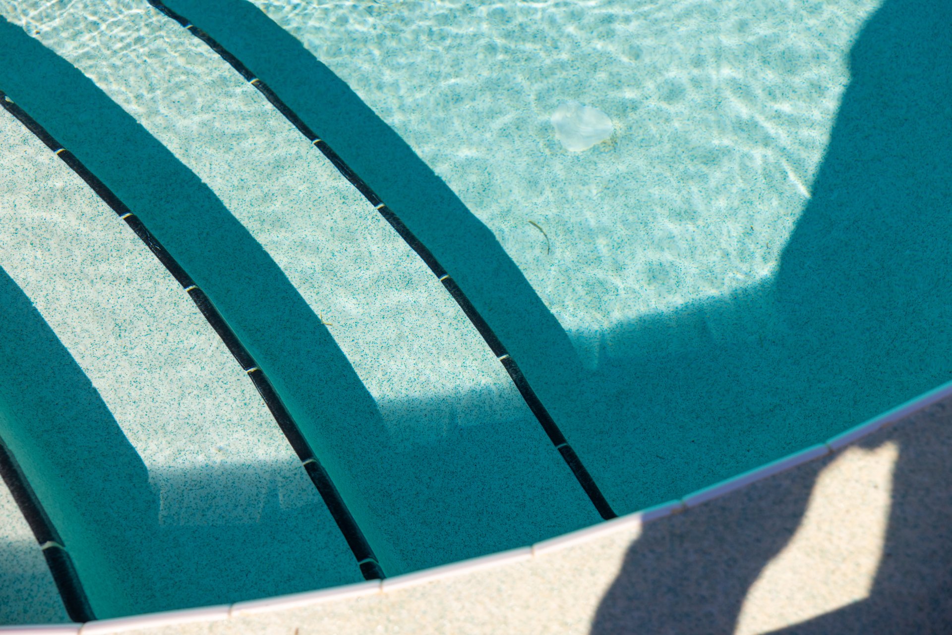 Sunlit pool steps with crystal-clear water and soft shadows, creating a calm, refreshing tropical resort vibe.