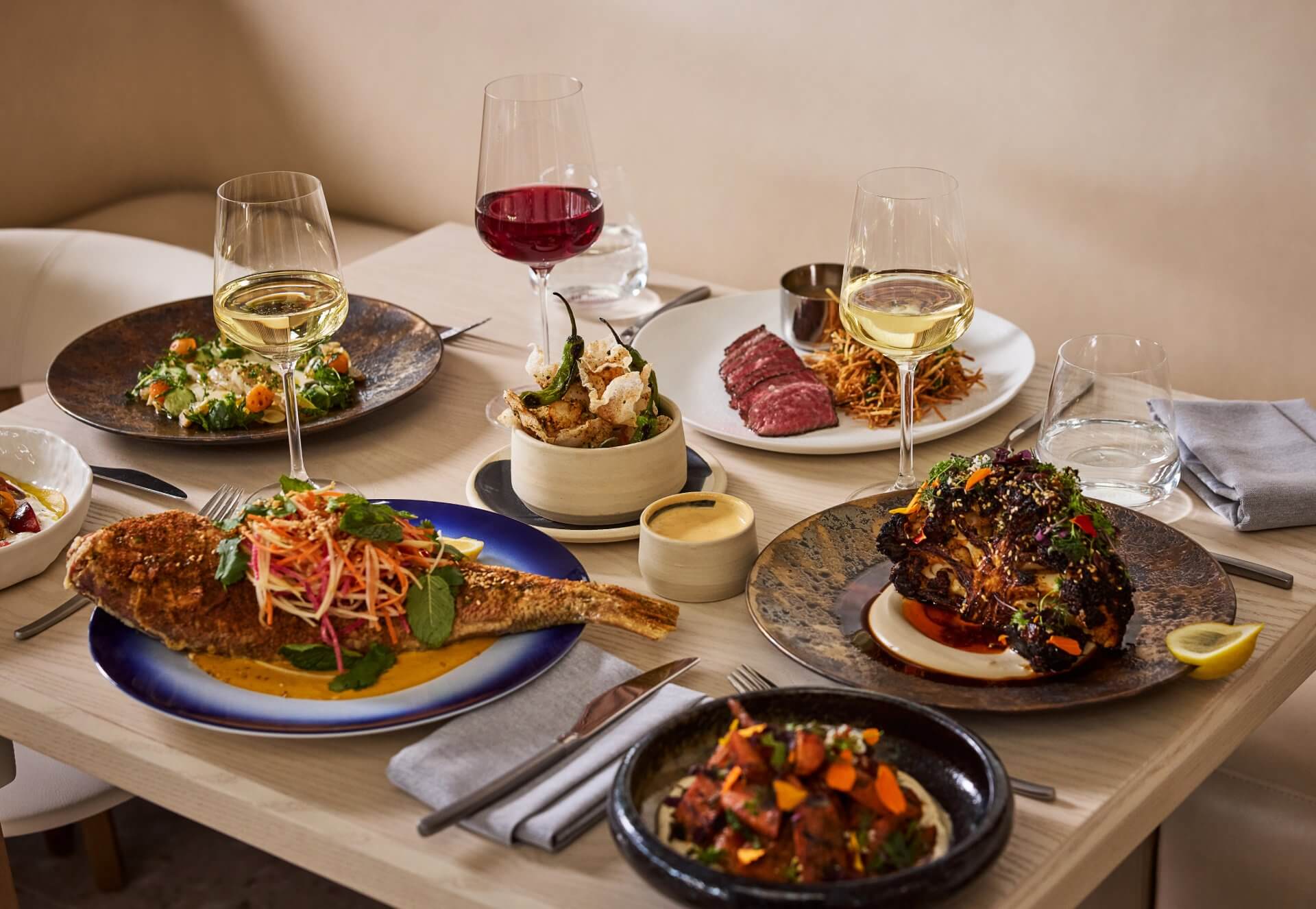 Elegant dining table with gourmet dishes and wine glasses, featuring seafood, steak, and artfully plated sides.