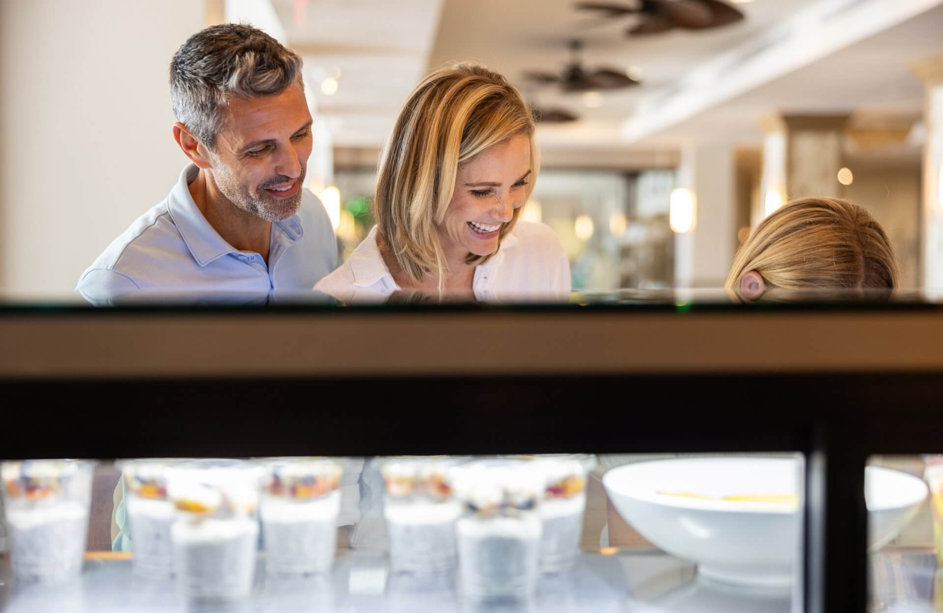 Family smiling while choosing desserts at a bright indoor buffet with glass display cases.