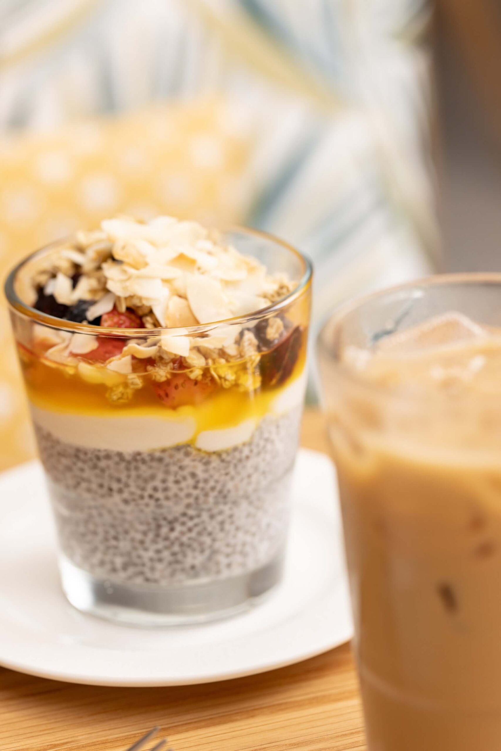 Chia pudding parfait layered with yogurt, fruit, granola, and coconut flakes, served with an iced coffee.