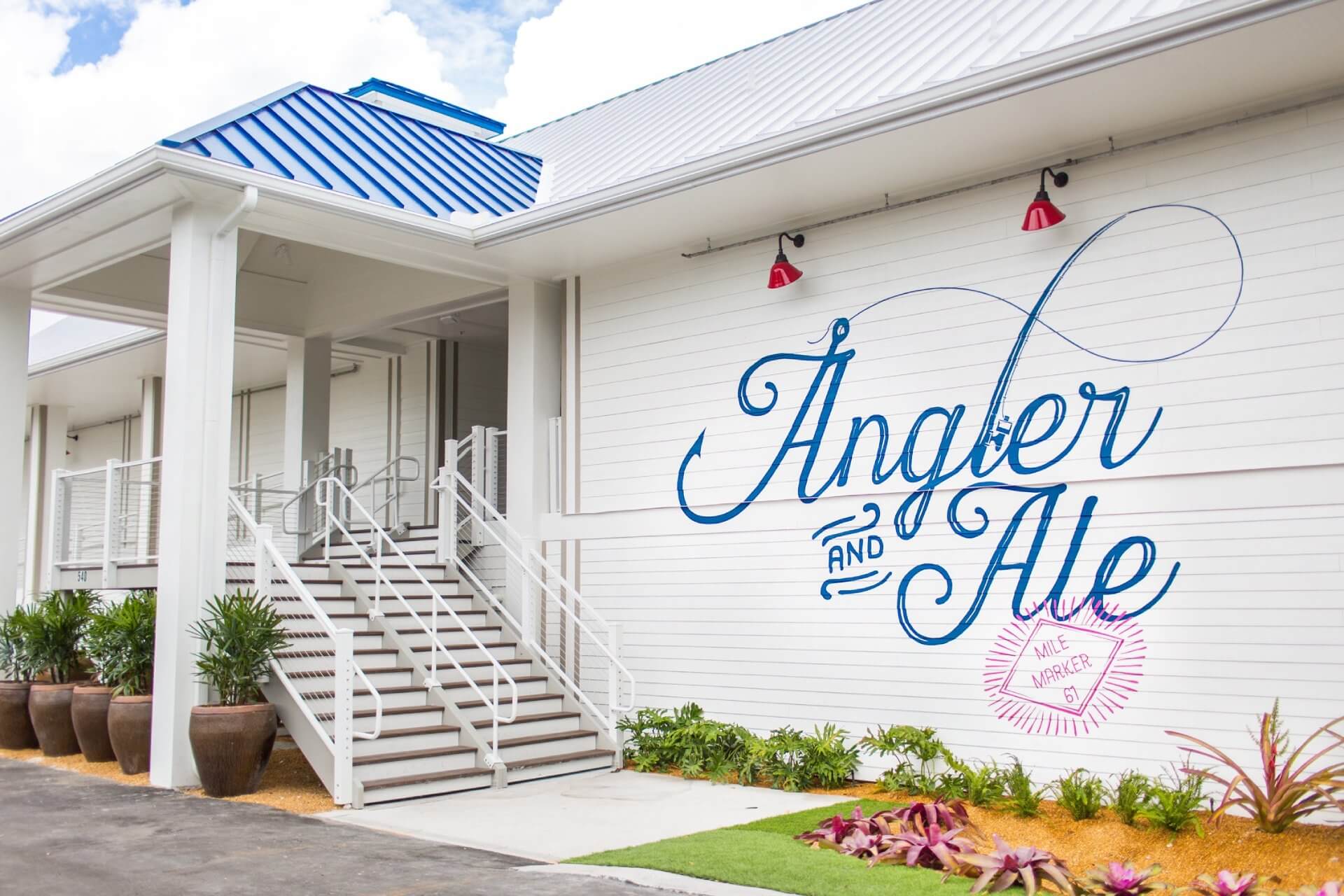 Exterior of Angler and Ale restaurant with white building, blue roof accents, stairs, and large painted logo.