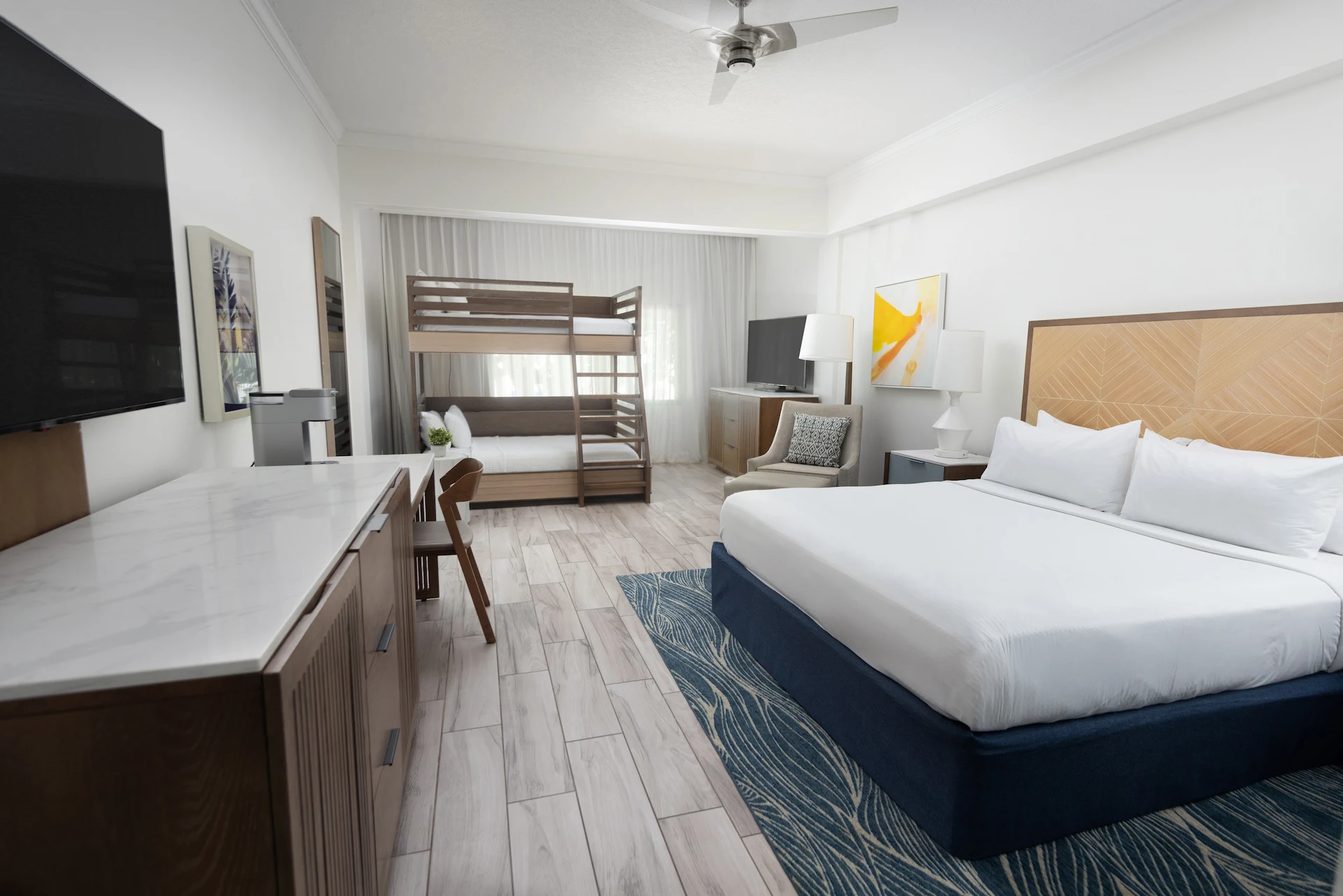 Spacious room with king bed, bunk beds, two TVs, and bright decor for a family stay.