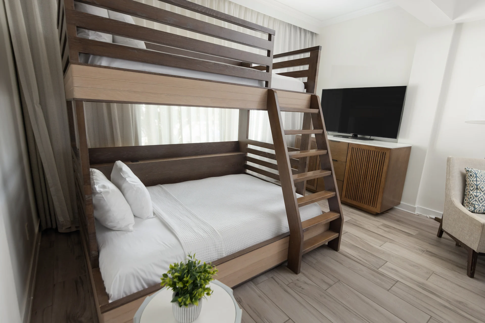 Neat bedroom with wood bunk bed, armchair, and TV cabinet in a bright, family-friendly space.