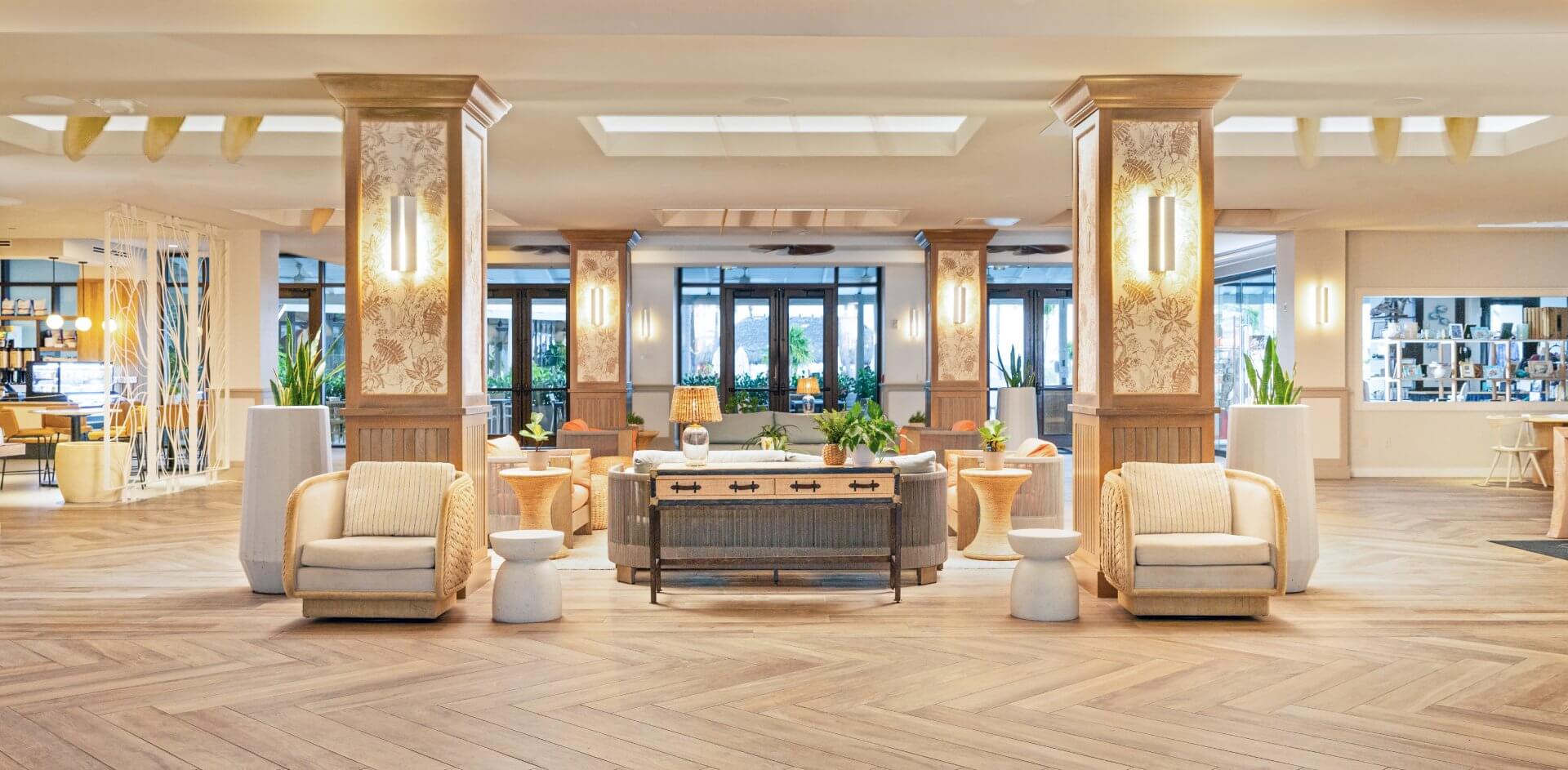 Bright resort lobby with cozy seating, natural wood accents, tropical plants, and warm lighting in an open, welcoming space.