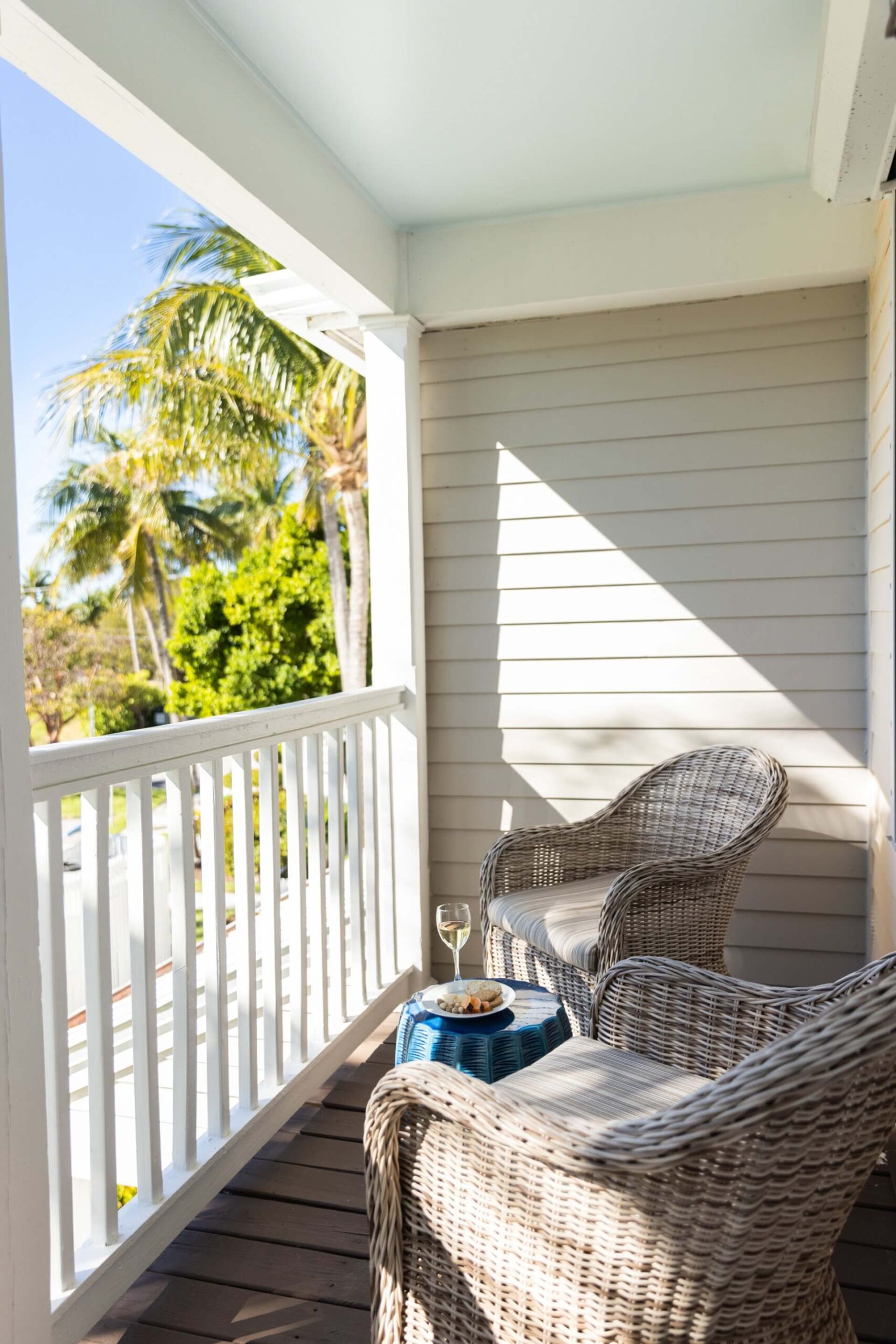 Private resort balcony with wicker chairs, a small table, and palm tree views in bright sunlight.
