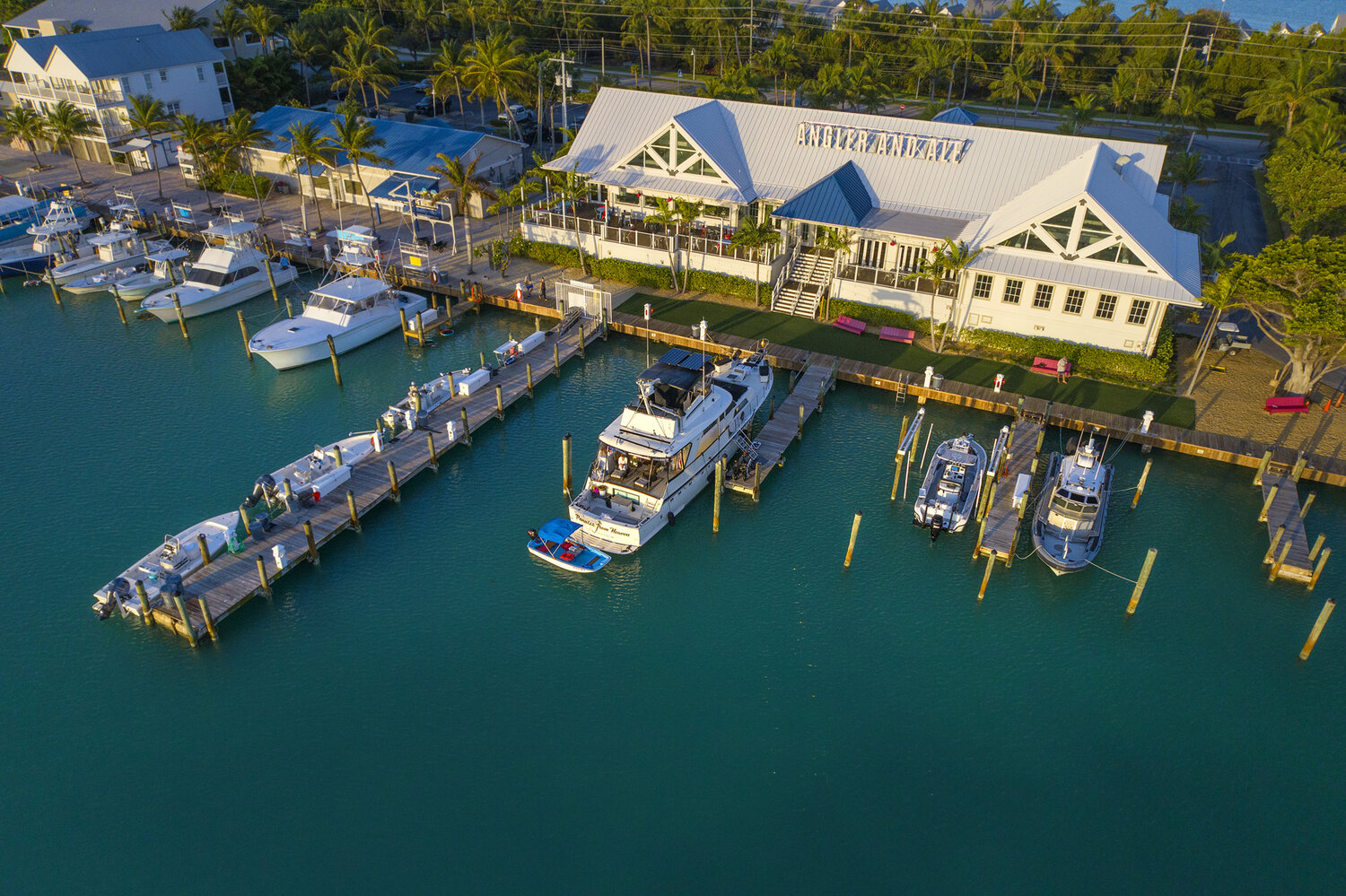 Aerial view of Angler & Ale waterfront restaurant with docked boats, marina slips, and palm-lined shoreline.