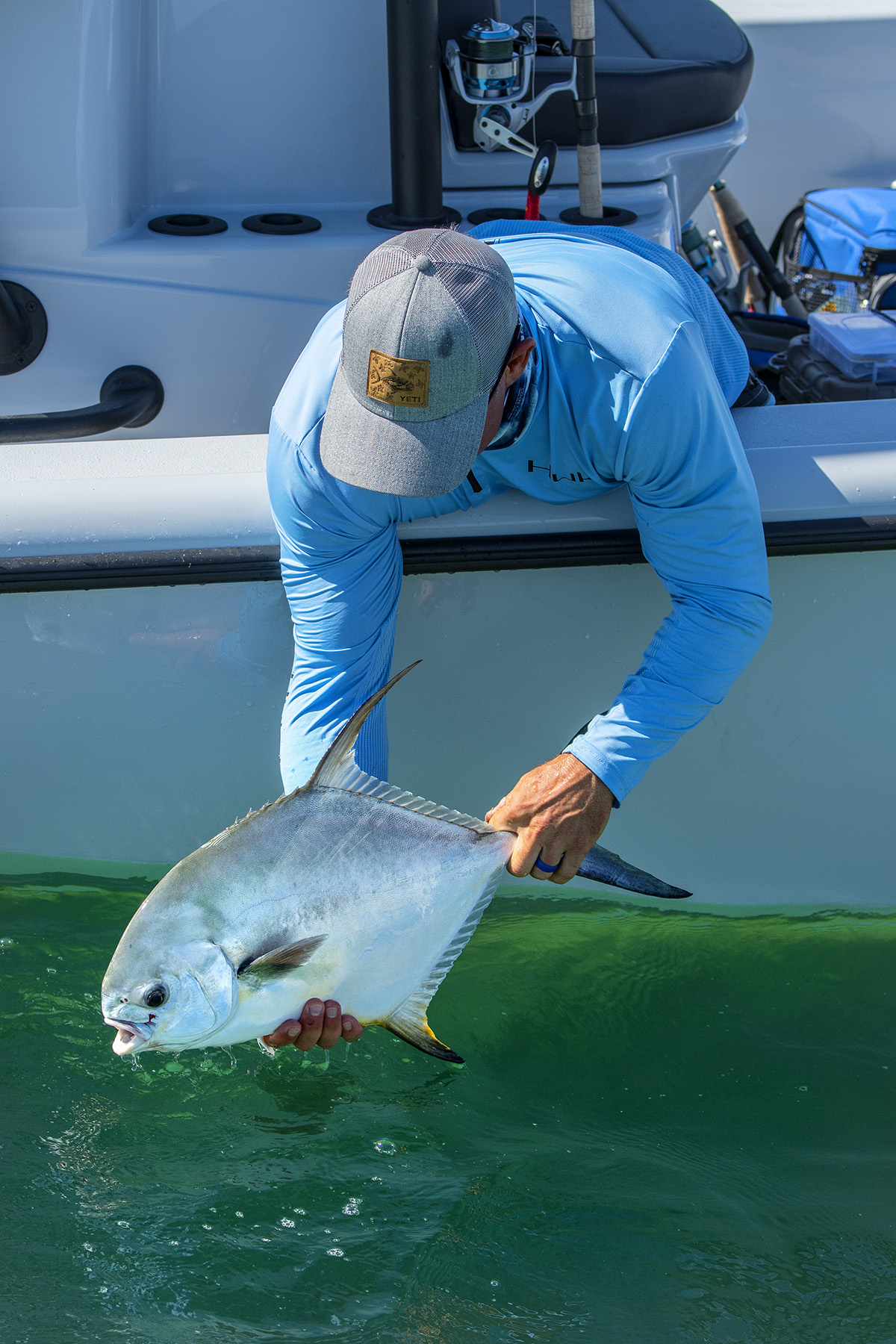 Angler on a boat carefully releasing a silver fish back into clear green water during a fishing trip.