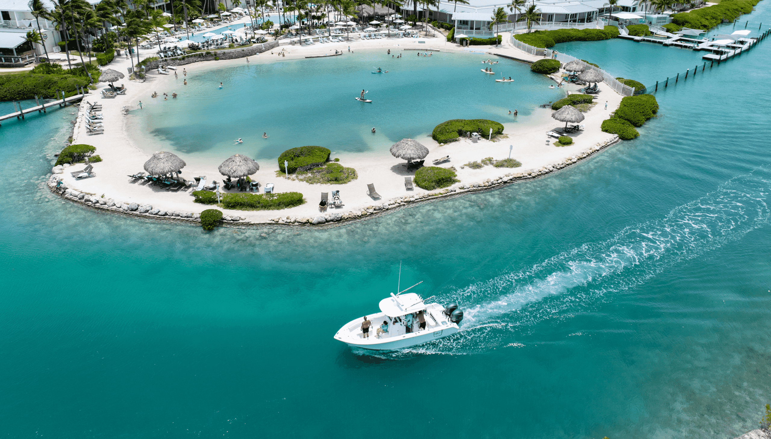 Aerial view of a white boat cruising turquoise waters near the tropical beach lagoon and villas at Hawks Cay Resort.